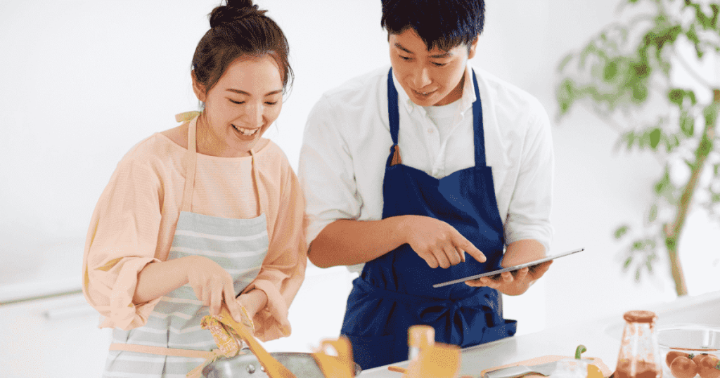 キッチンでタブレットを見ながら料理をする二人