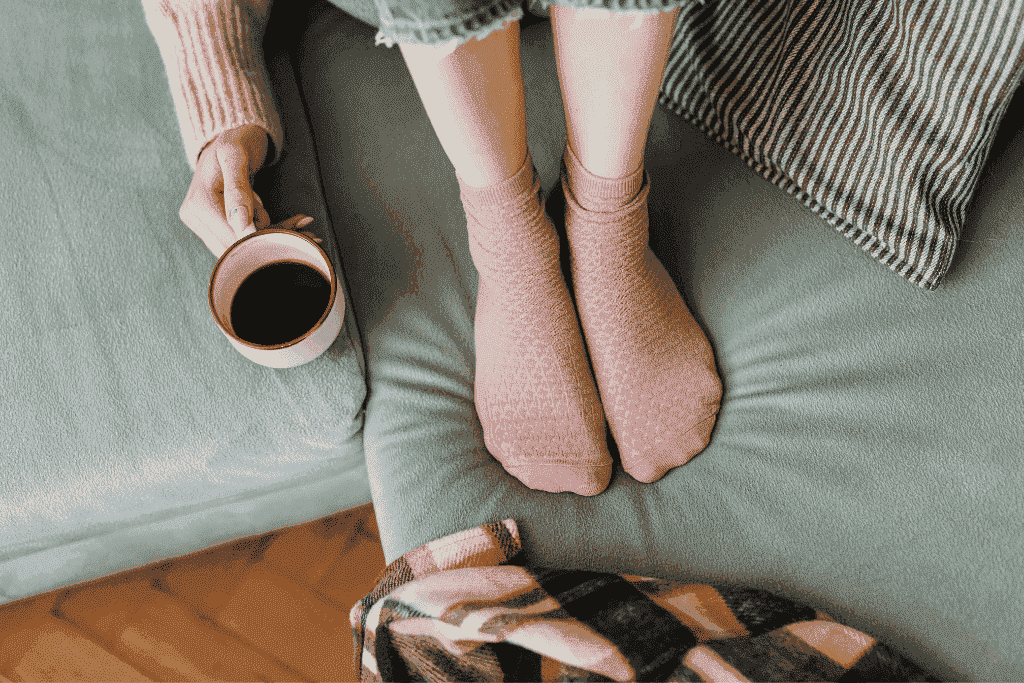 ピンクの靴下を履いた足とコーヒーを持つ手がソファの上にある様子