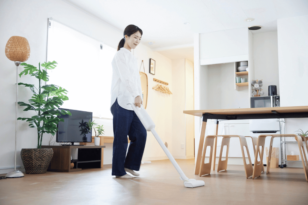 明るい部屋でスティック掃除機を使う女性